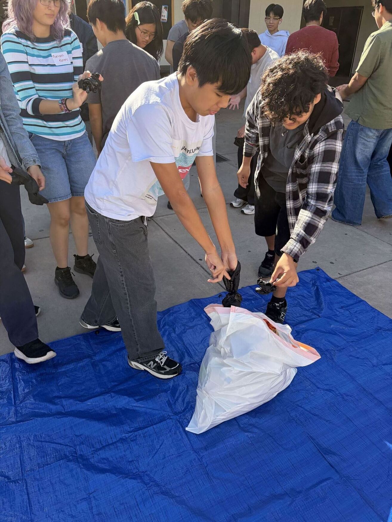 Two students removing black gloves into a trash bag.