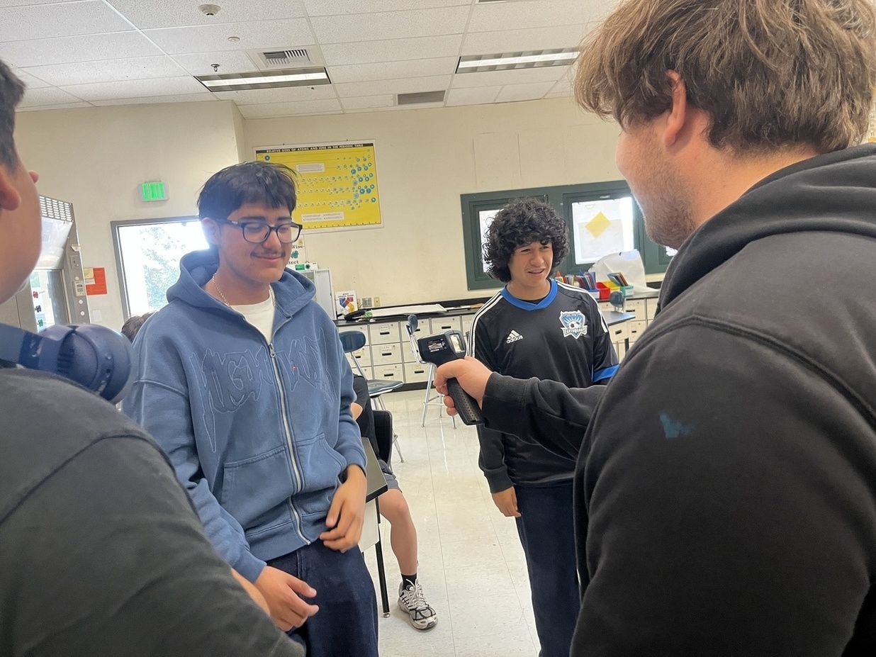 Student pointing an IR thermometer at another student.